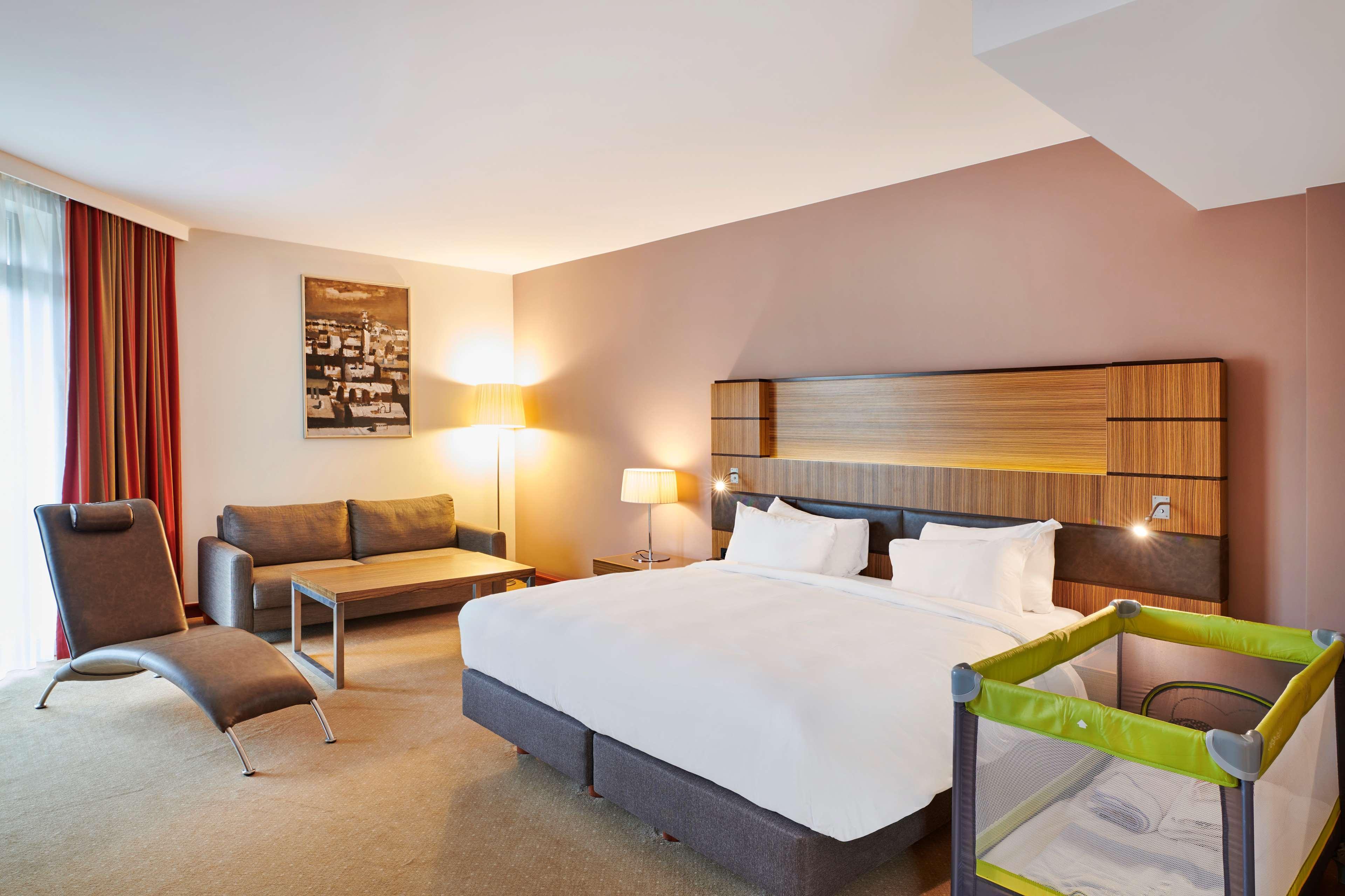 Radisson Blu Hotel Cracovia Esterno foto The photo shows a hotel room that features a spacious layout. There is a large bed with white linens positioned against a modern headboard. To one side, there is a cozy seating area with a small coffee table and a sofa. A stylish floor lamp provides 