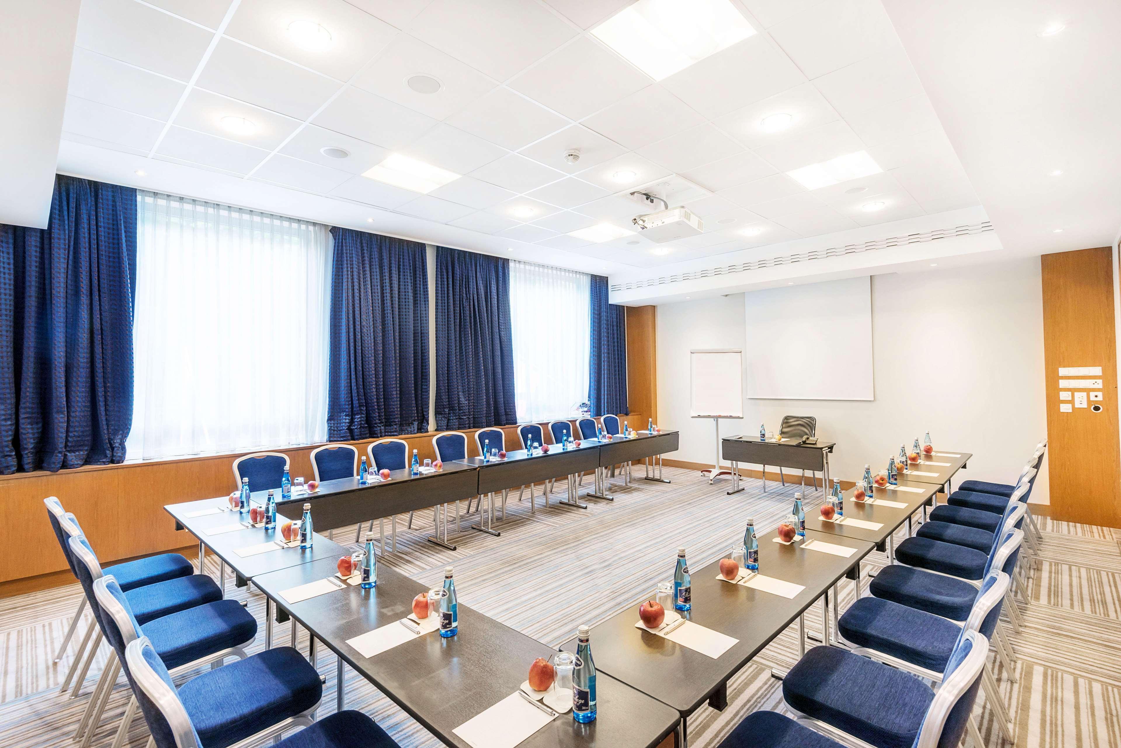 Radisson Blu Hotel Cracovia Esterno foto The photo shows a modern conference room arranged for a meeting. In the center, there is a long rectangular table surrounded by chairs. Each place at the table has a small water bottle and what appears to be a notepad or menu. The room is well-lit wi