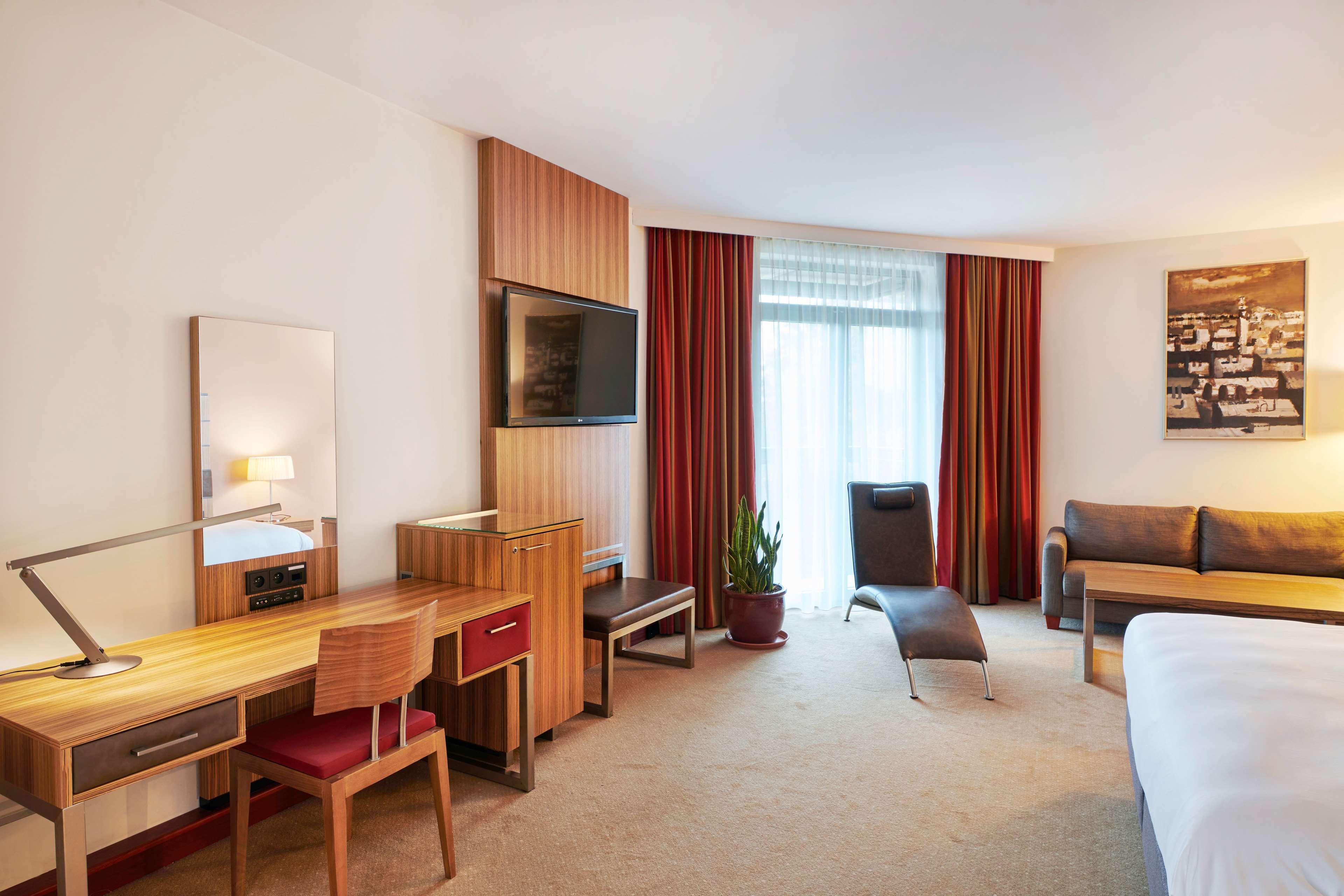 Radisson Blu Hotel Cracovia Esterno foto The photo shows a hotel room that features a modern and comfortable layout. It includes a double bed, a seating area with a sofa, and a large window covered by sheer and dark curtains, allowing natural light to enter the space. There is a wooden desk