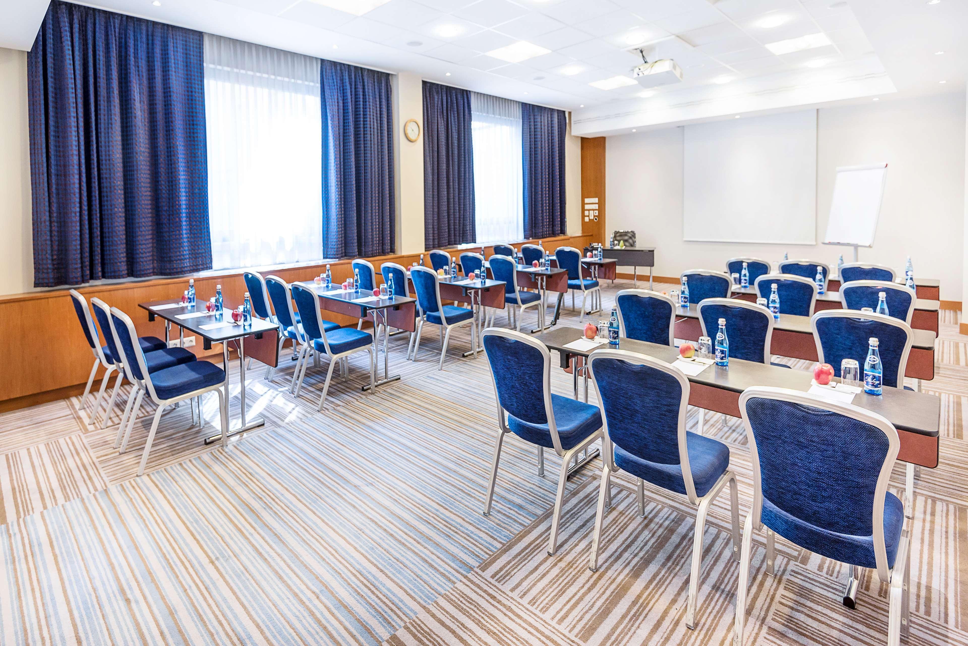 Radisson Blu Hotel Cracovia Esterno foto The photo shows a conference or meeting room setup. There are several rows of tables arranged with blue chairs around them. The room is well-lit, featuring large windows with dark curtains. A whiteboard or projection screen is visible at one end of t