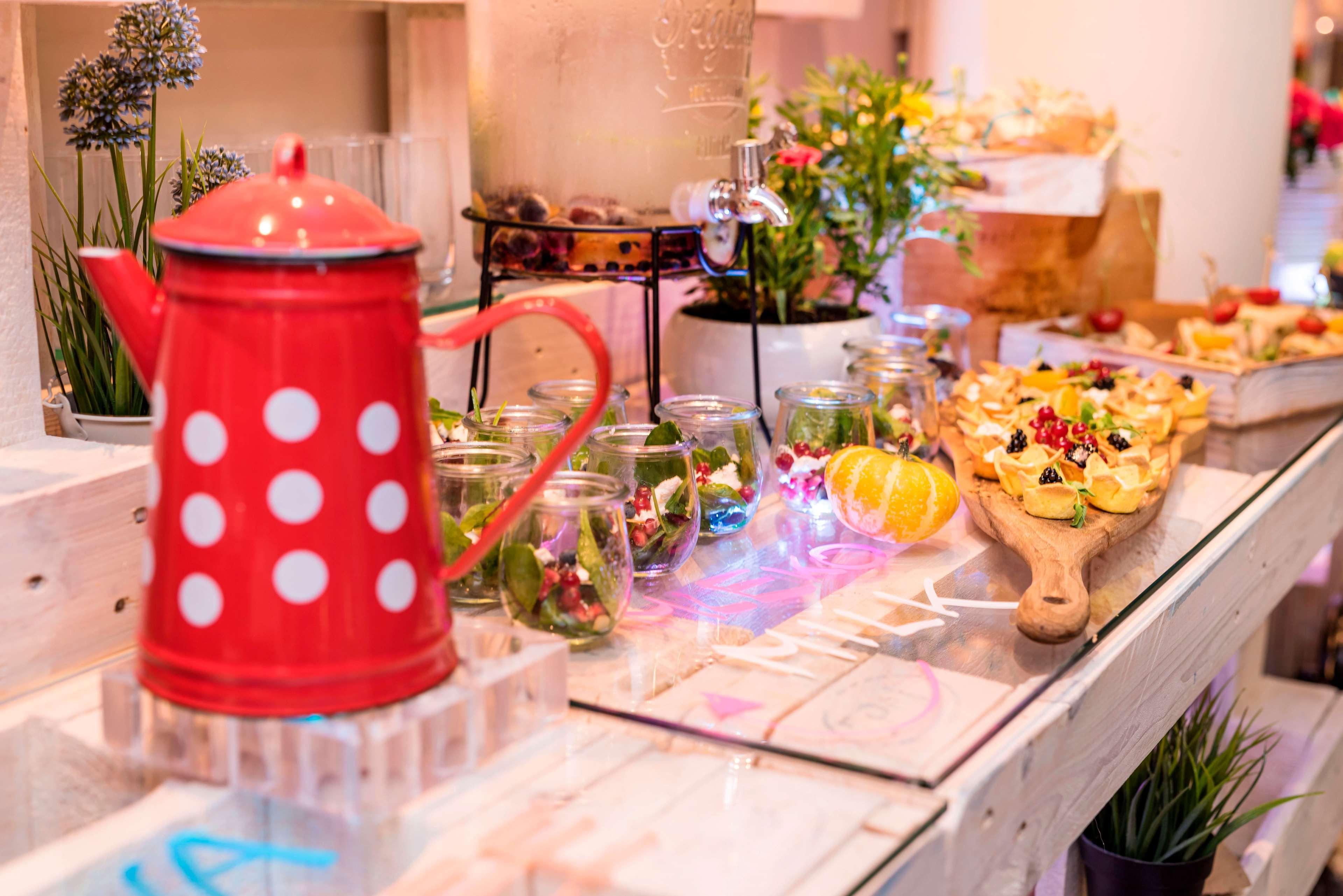 Radisson Blu Hotel Cracovia Esterno foto The photo displays a colorful food and drink setup. Prominently featured is a red kettle with white polka dots, placed on a clear stand. Surrounding the kettle are glass jars filled with vibrant greenery, possibly salads or herbal arrangements. There