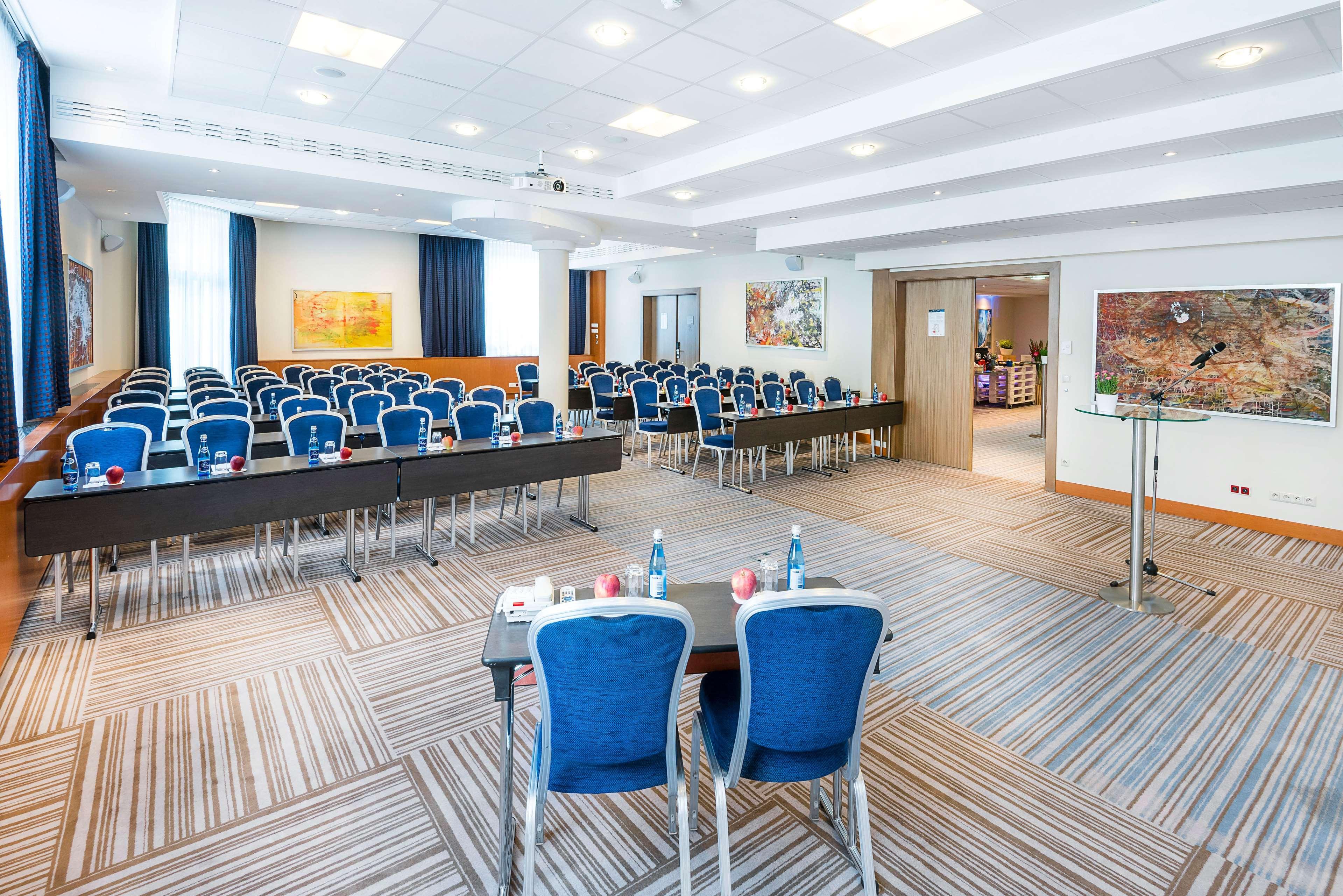 Radisson Blu Hotel Cracovia Esterno foto The photo shows a conference room set up for a meeting or seminar. It features multiple rows of blue chairs arranged behind long tables. The room is well-lit with natural light coming from large windows, and there are decorative artworks on the walls