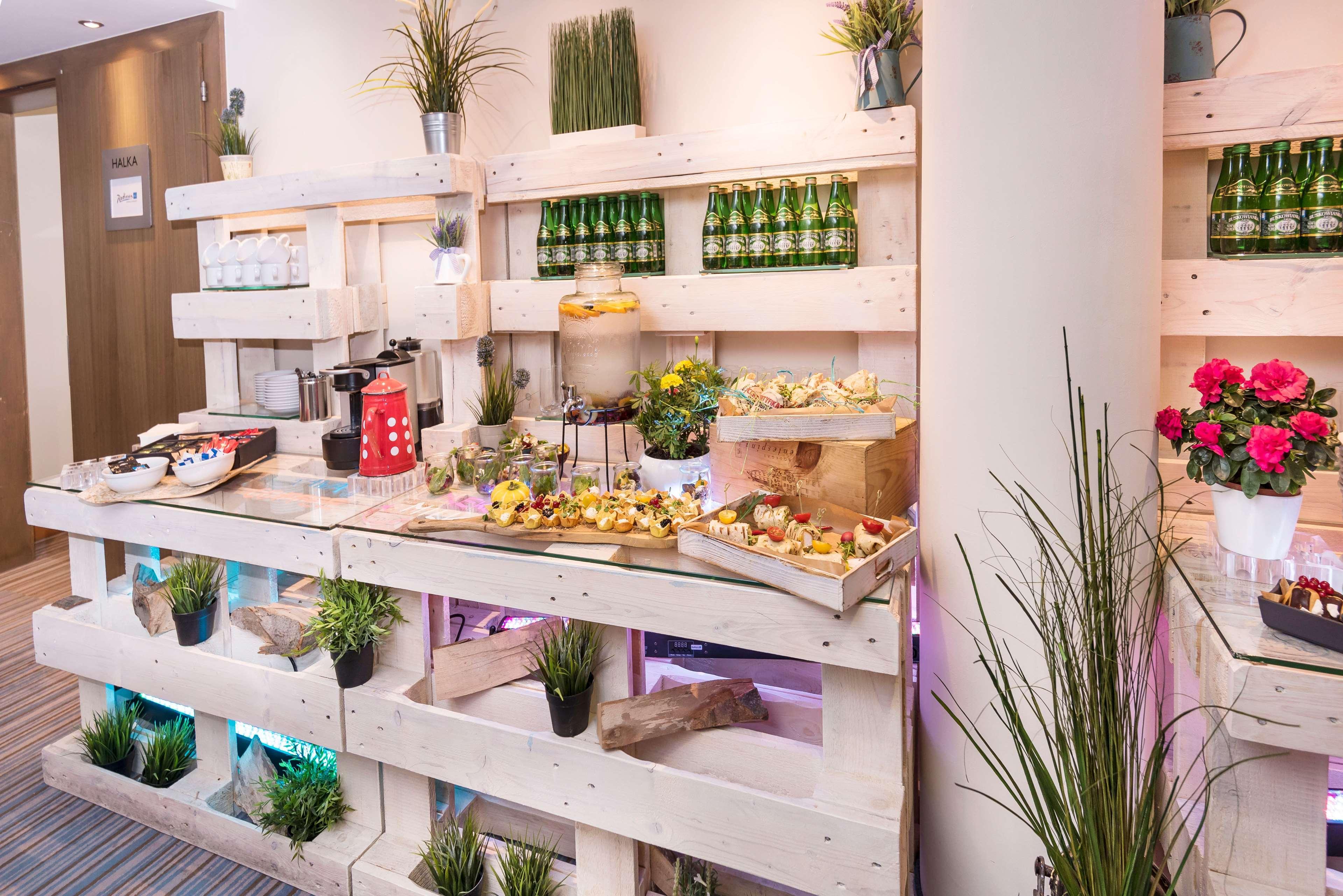 Radisson Blu Hotel Cracovia Esterno foto The photo shows a stylish buffet or food display area made from wooden pallets. It features various food items, including pastries and small dishes, arranged neatly on the shelves. There are decorative elements like potted plants and artificial grass