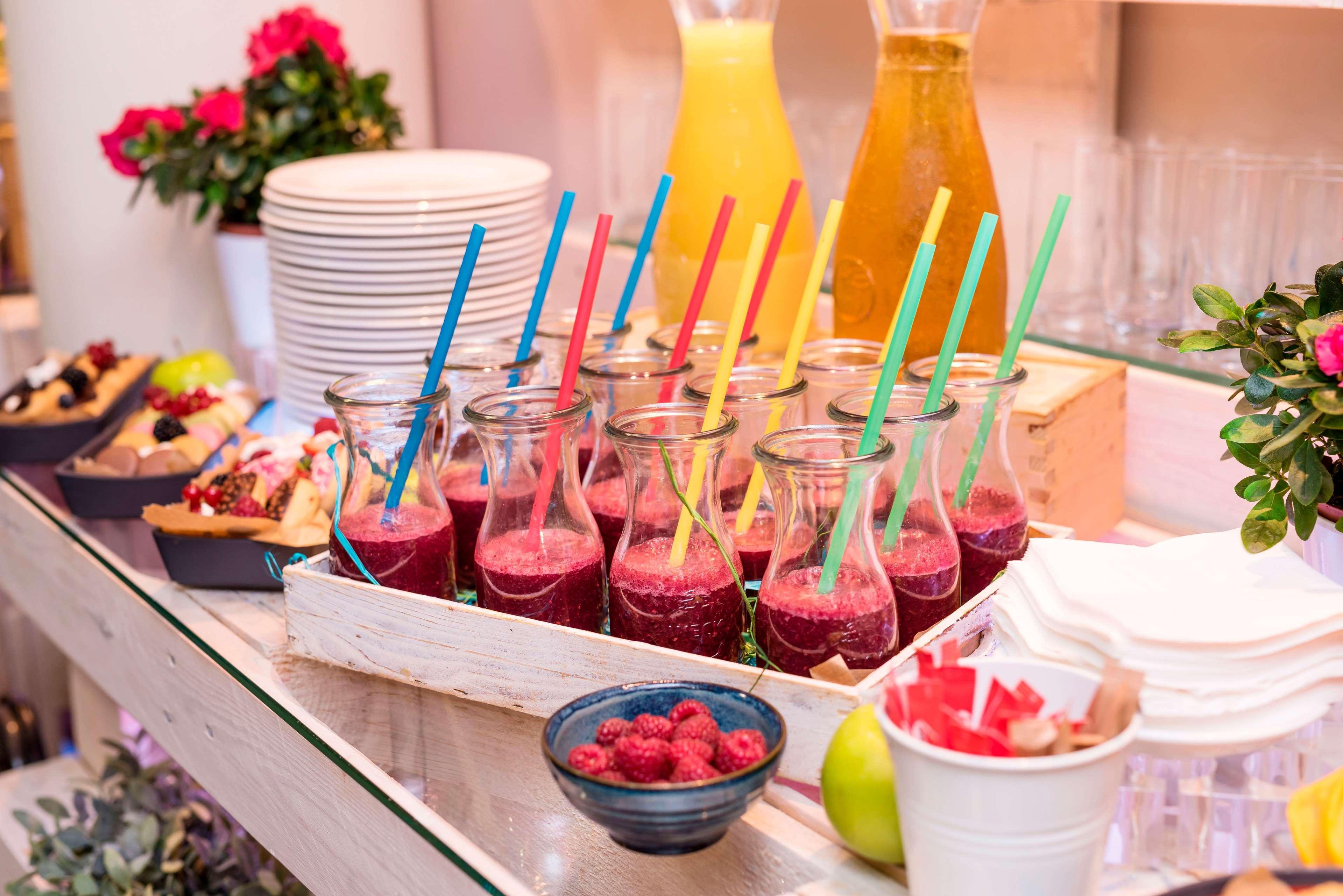 Radisson Blu Hotel Cracovia Esterno foto The photo depicts a colorful beverage display. There are several small glass bottles filled with a deep red smoothie or juice, each equipped with a colorful straw. Next to these bottles, there is a bowl of fresh raspberries. In the background, there 