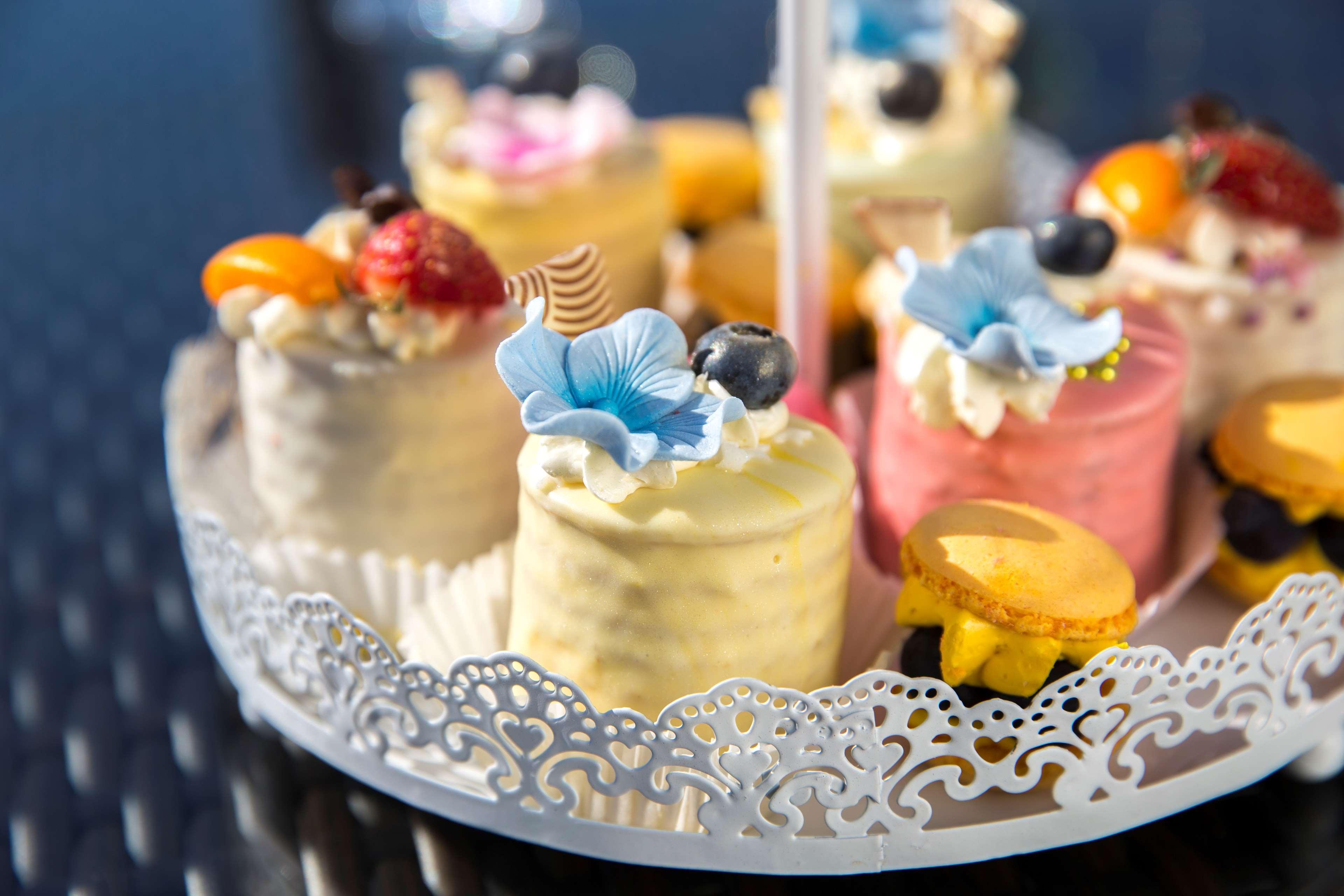 Radisson Blu Hotel Cracovia Esterno foto The photo shows a decorative platter filled with small, colorful cakes or pastries. Each cake is topped with various decorations, including edible flowers, fruits, and cream. The cakes appear to be in different shades, such as yellow, pink, and white