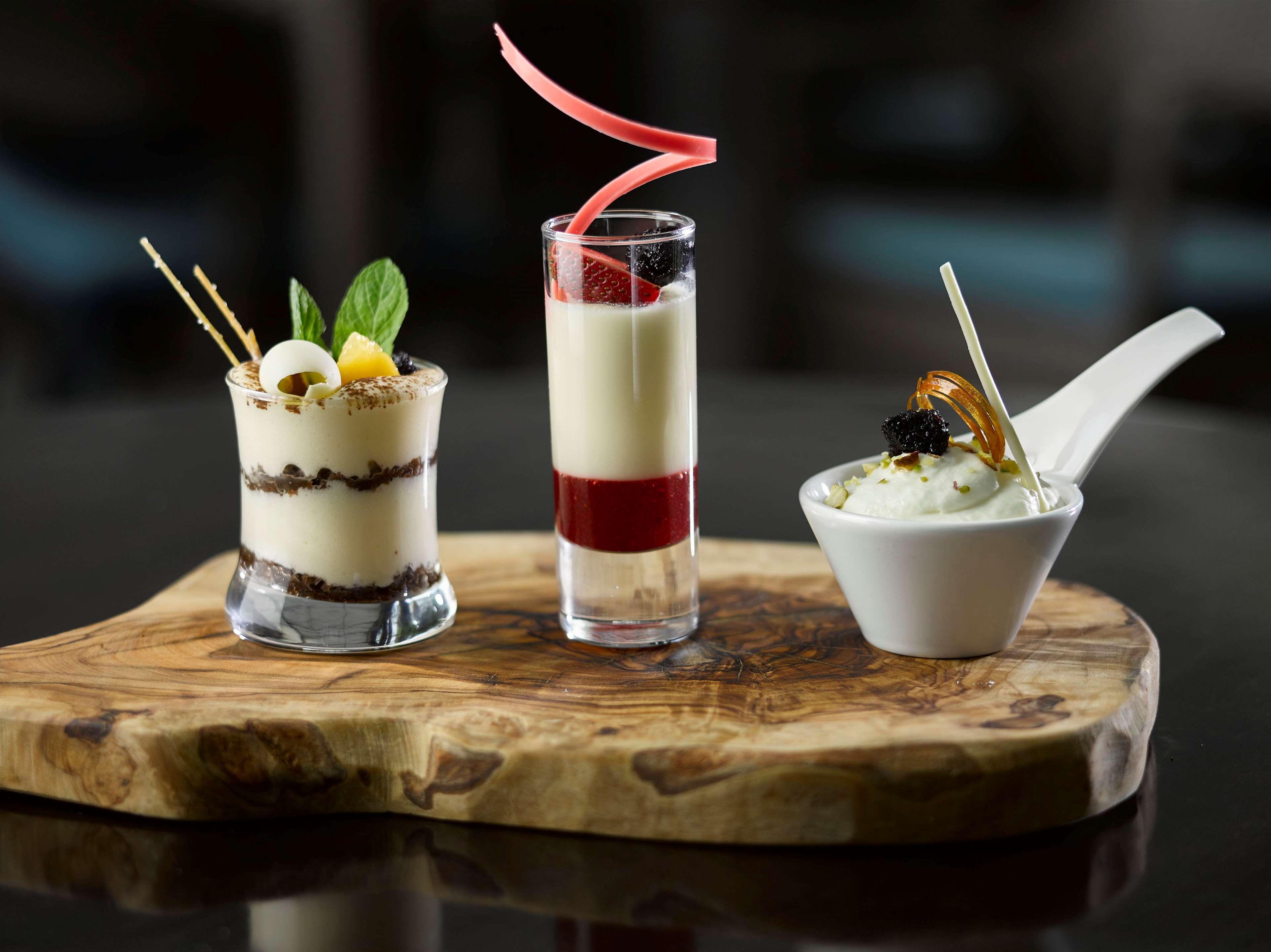 Radisson Blu Hotel Cracovia Esterno foto The photo features a platter with three distinct desserts, elegantly presented on a wooden board:

1. **First Dessert**: A glass dessert with layers of cream and chocolate, topped with small fruits and adorned with mint leaves and decorative sticks.
