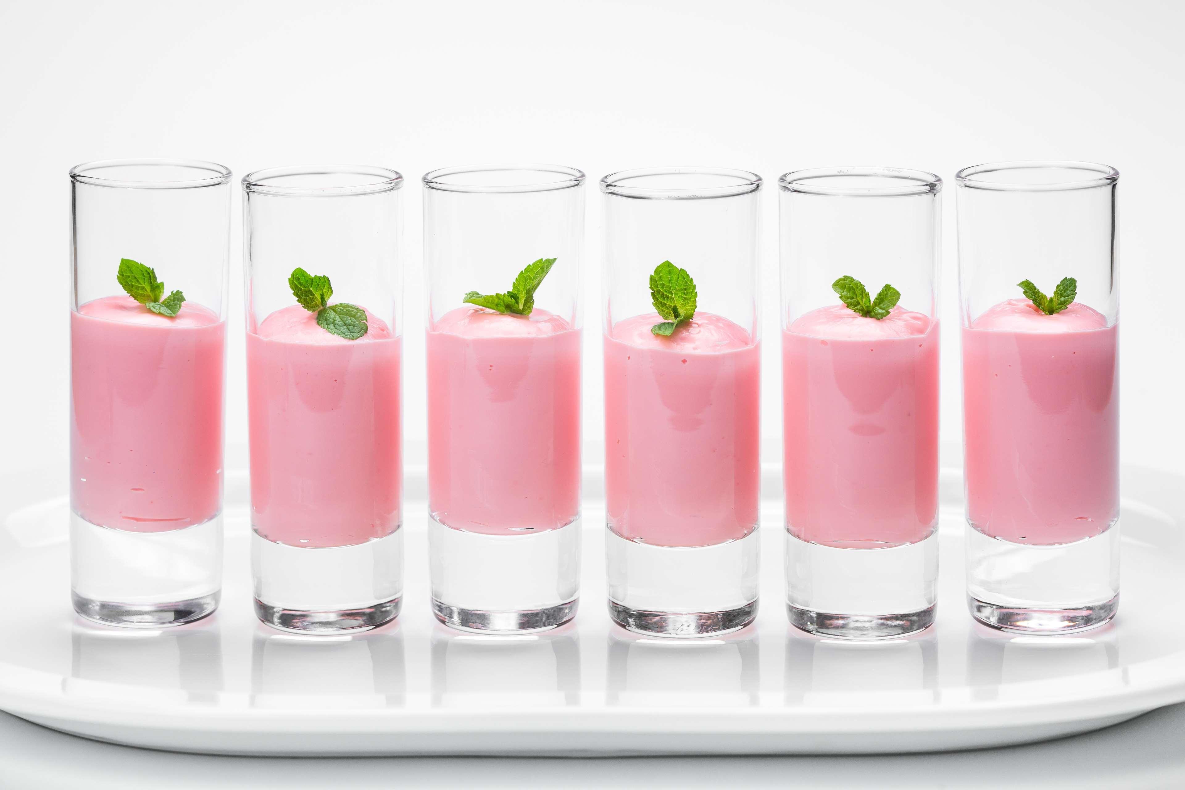 Radisson Blu Hotel Cracovia Esterno foto The photo shows a row of six clear shot glasses filled with a pink creamy dessert or drink. Each glass is topped with a small sprig of fresh mint, giving a decorative touch. The glasses are arranged neatly on a white plate, creating a clean and appea