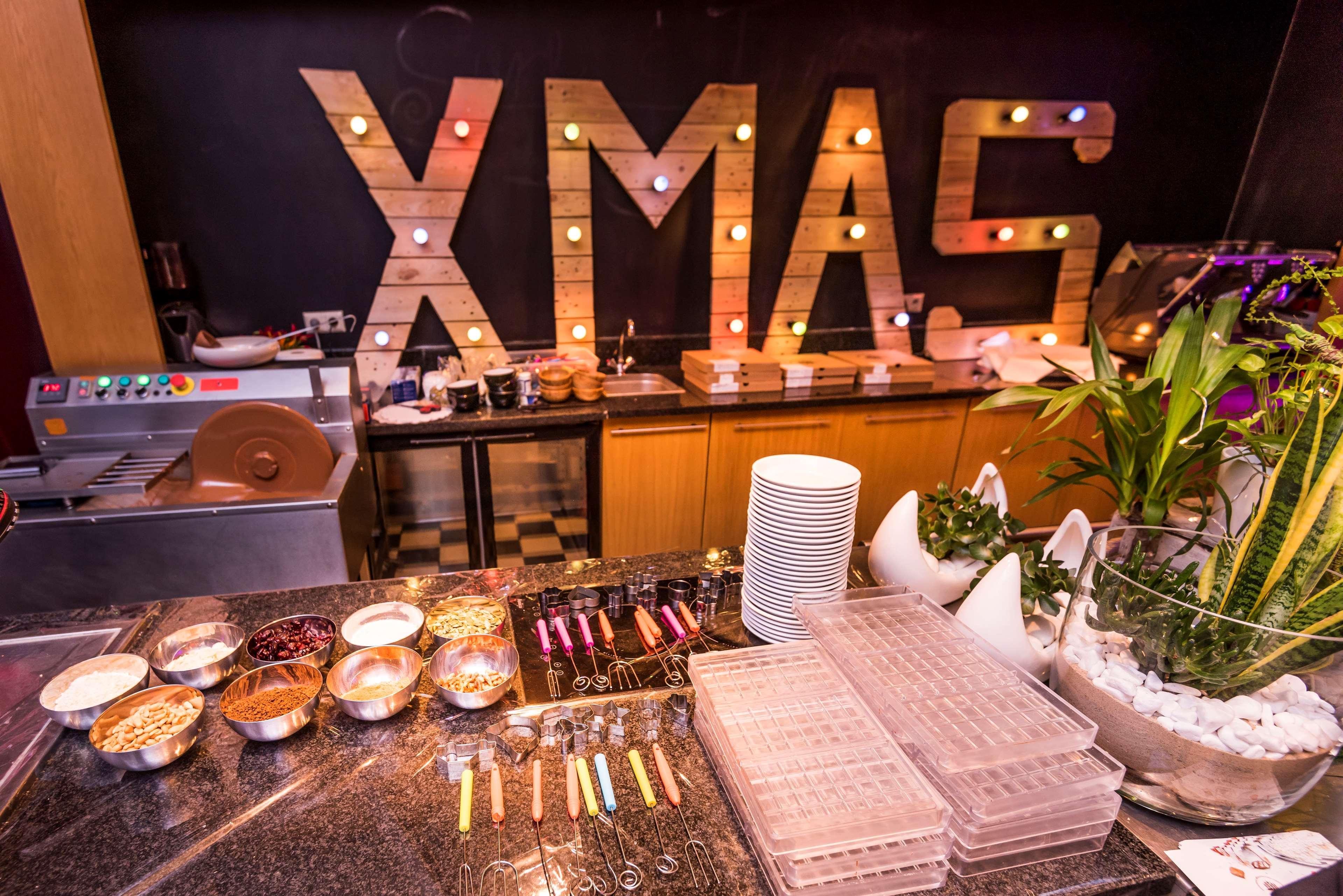 Radisson Blu Hotel Cracovia Esterno foto The photo shows a festive setting with a prominent display featuring the word "XMAS" made of wooden letters illuminated by colorful lights. In the foreground, there's a buffet-style table set up, displaying various bowls containing food items, possib