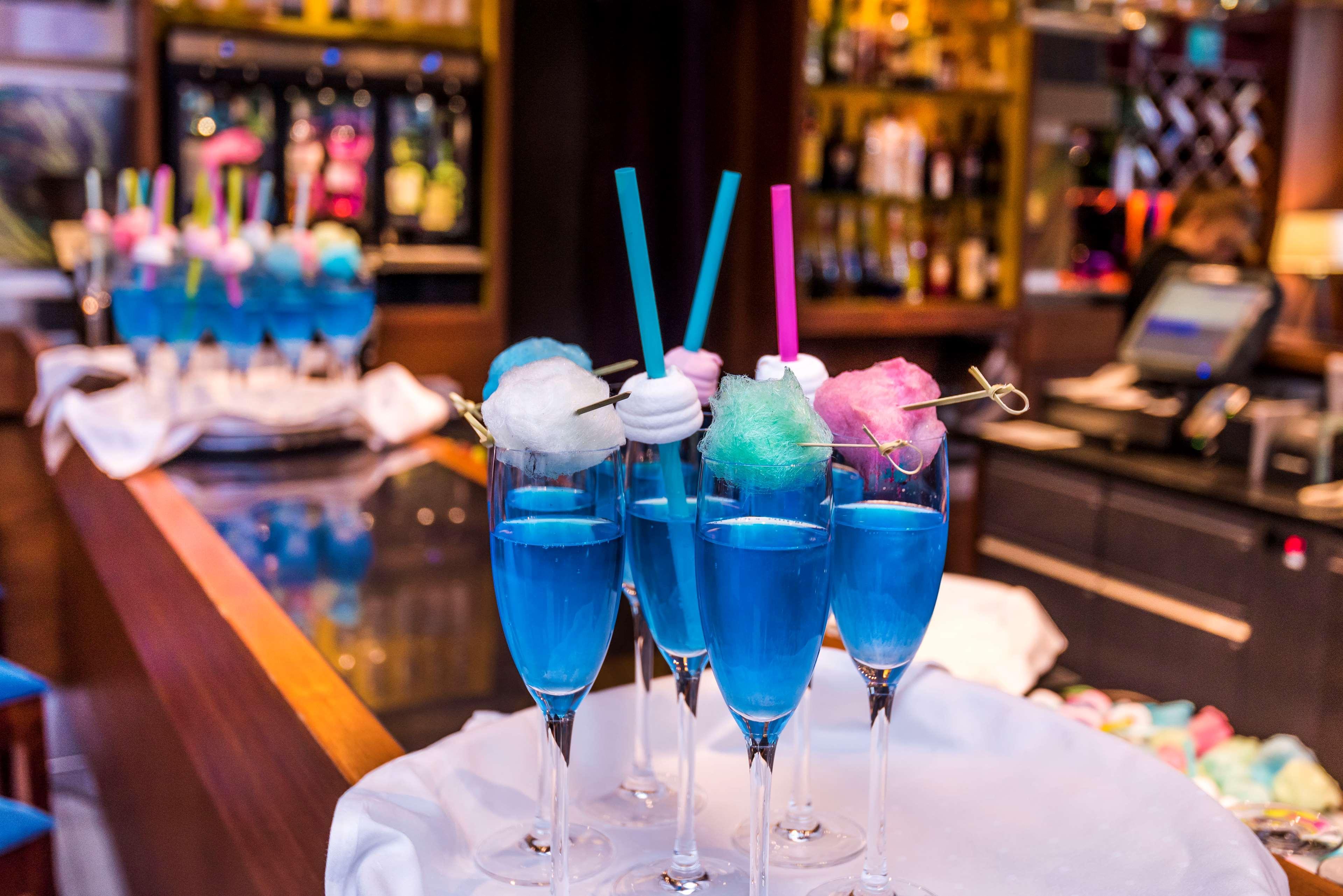 Radisson Blu Hotel Cracovia Esterno foto The photo shows a vibrant display of cocktails in tall glasses. Each drink is bright blue and garnished with colorful cotton candy on top, creating a whimsical appearance. Some glasses have straws—one pink and one blue—adding to the playful presentat