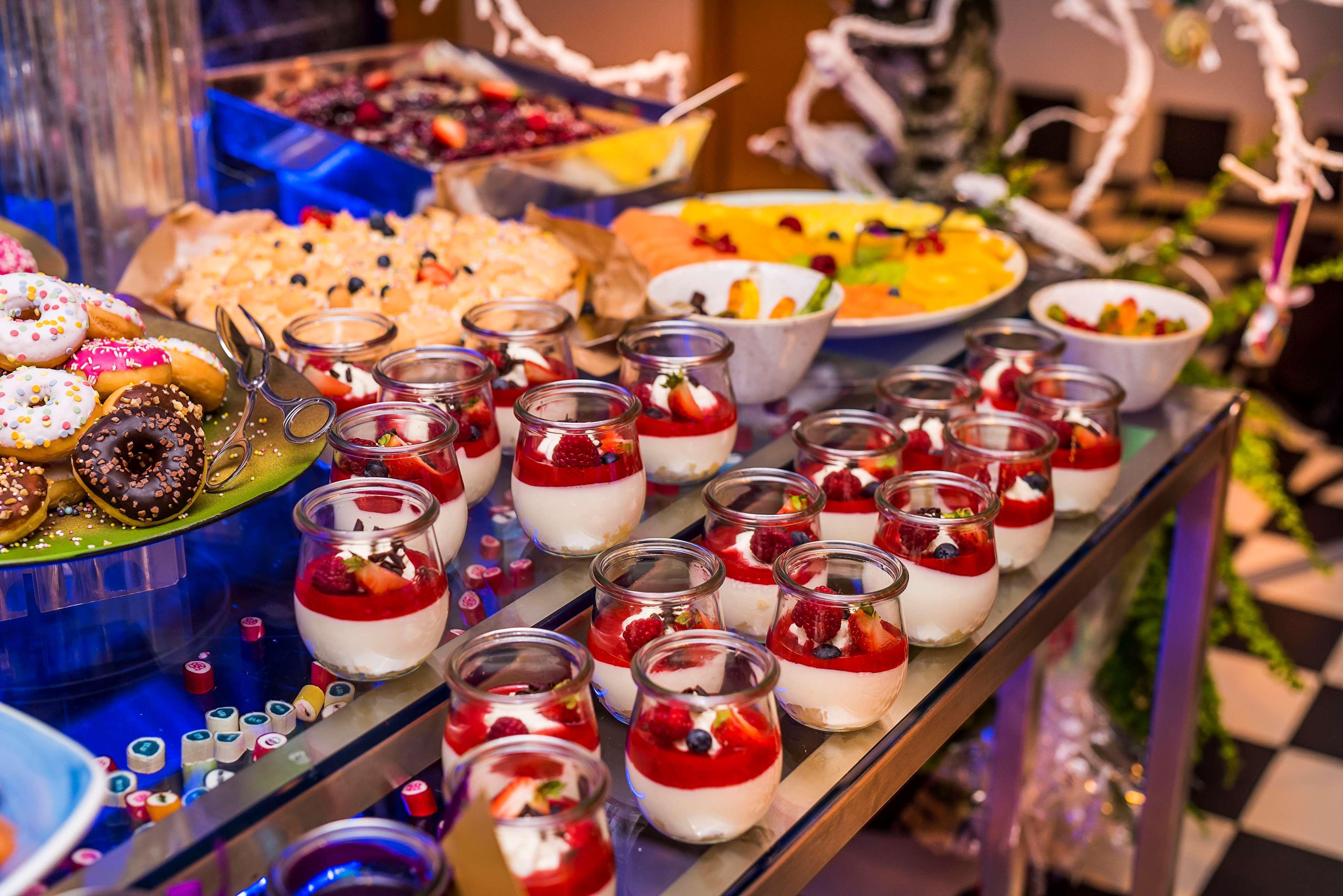 Radisson Blu Hotel Cracovia Esterno foto The image displays an array of desserts beautifully arranged on a table. In the foreground, there are small glass containers filled with a layered dessert, featuring a white creamy base topped with red fruit and garnished with berries. In the backgro