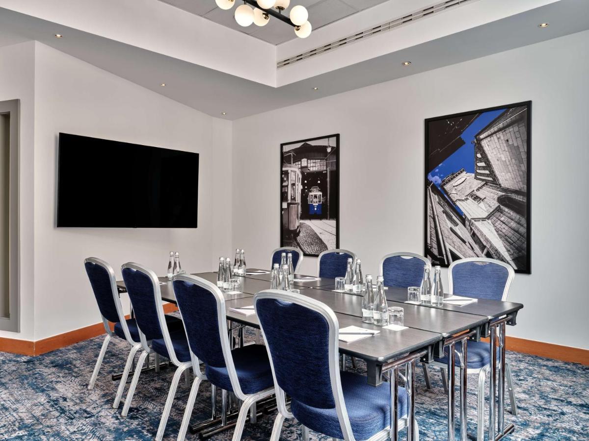 Radisson Blu Hotel Cracovia Esterno foto The photo depicts a modern conference room. It features a long rectangular table with several blue upholstered chairs arranged around it. On the table are glass water bottles and glasses, suggesting a setup for a meeting or presentation. The room has