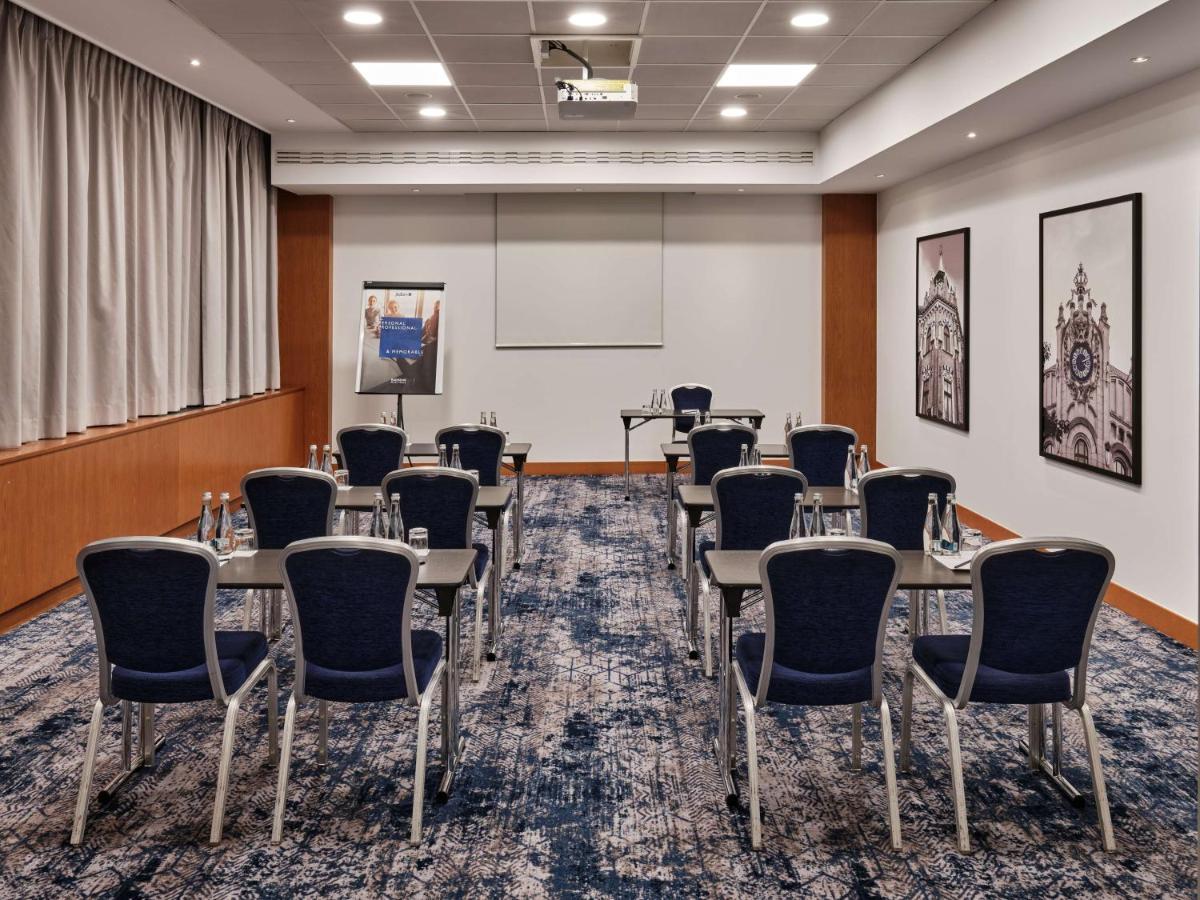 Radisson Blu Hotel Cracovia Esterno foto The photo shows a conference room set up for a meeting or presentation. The room features a light-colored carpet with a patterned design. There are several rows of chairs arranged facing a small table, which has water bottles on it. A flip chart stan