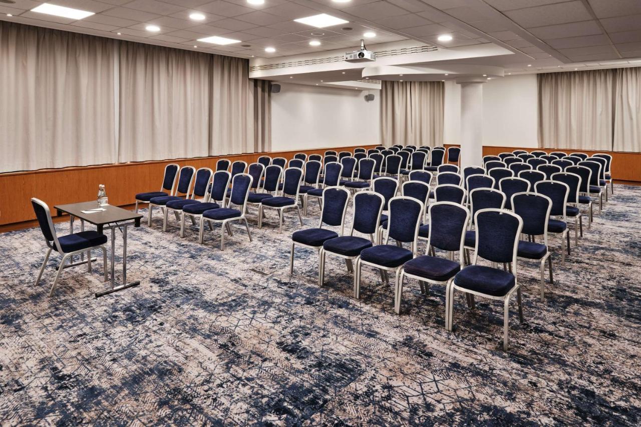 Radisson Blu Hotel Cracovia Esterno foto The photo shows a conference room set up for a meeting or event. There are rows of blue chairs arranged neatly, indicating a capacity for attendees. At the front of the room, there is a small table, likely for speakers or presenters, alongside a wate