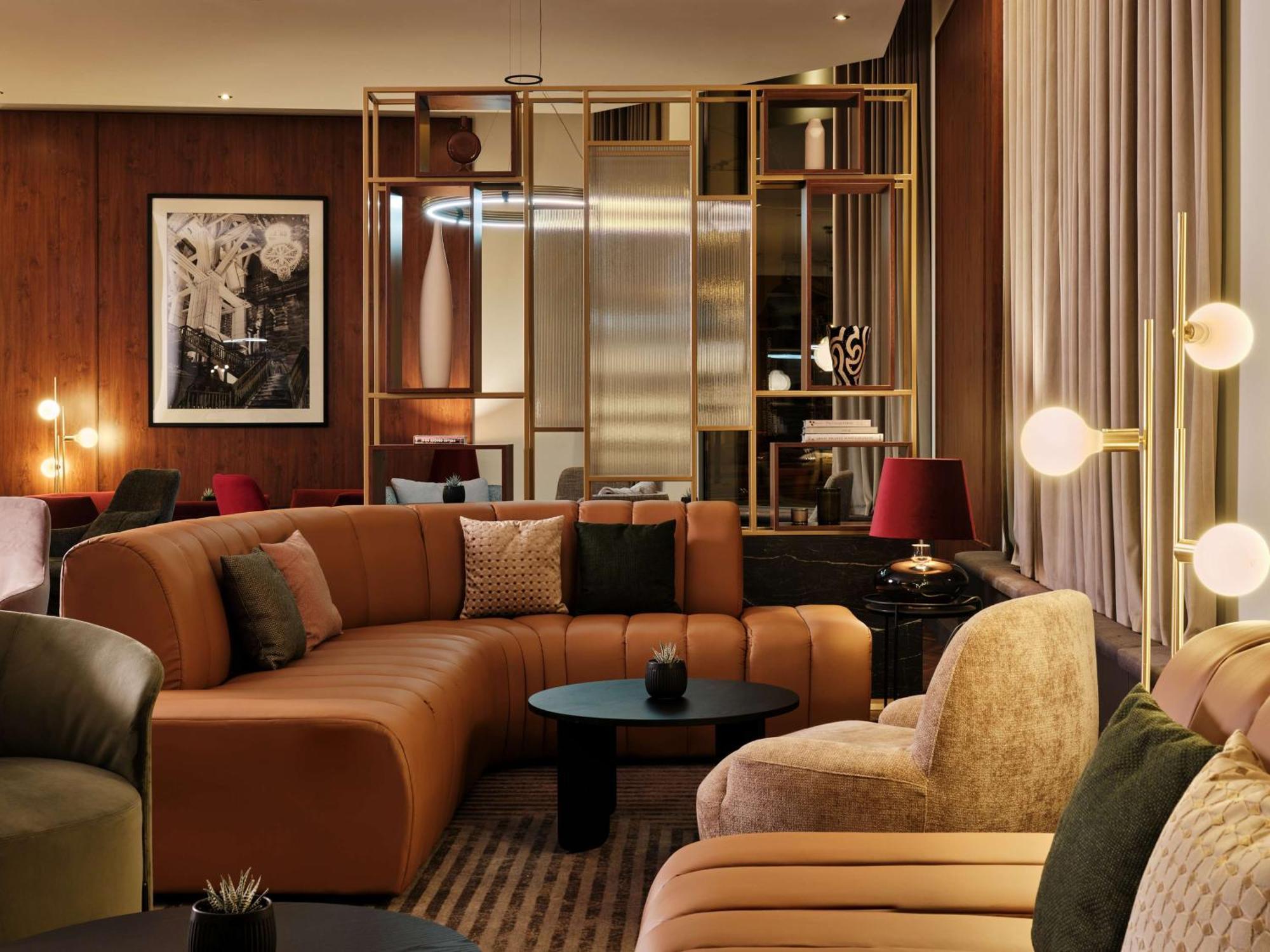 Radisson Blu Hotel Cracovia Esterno foto The photo shows a modern and stylish lounge area. It features a curved, multi-colored sectional sofa with a combination of beige, brown, and green upholstery. There are various decorative cushions on the sofa, adding a touch of comfort. In front of t