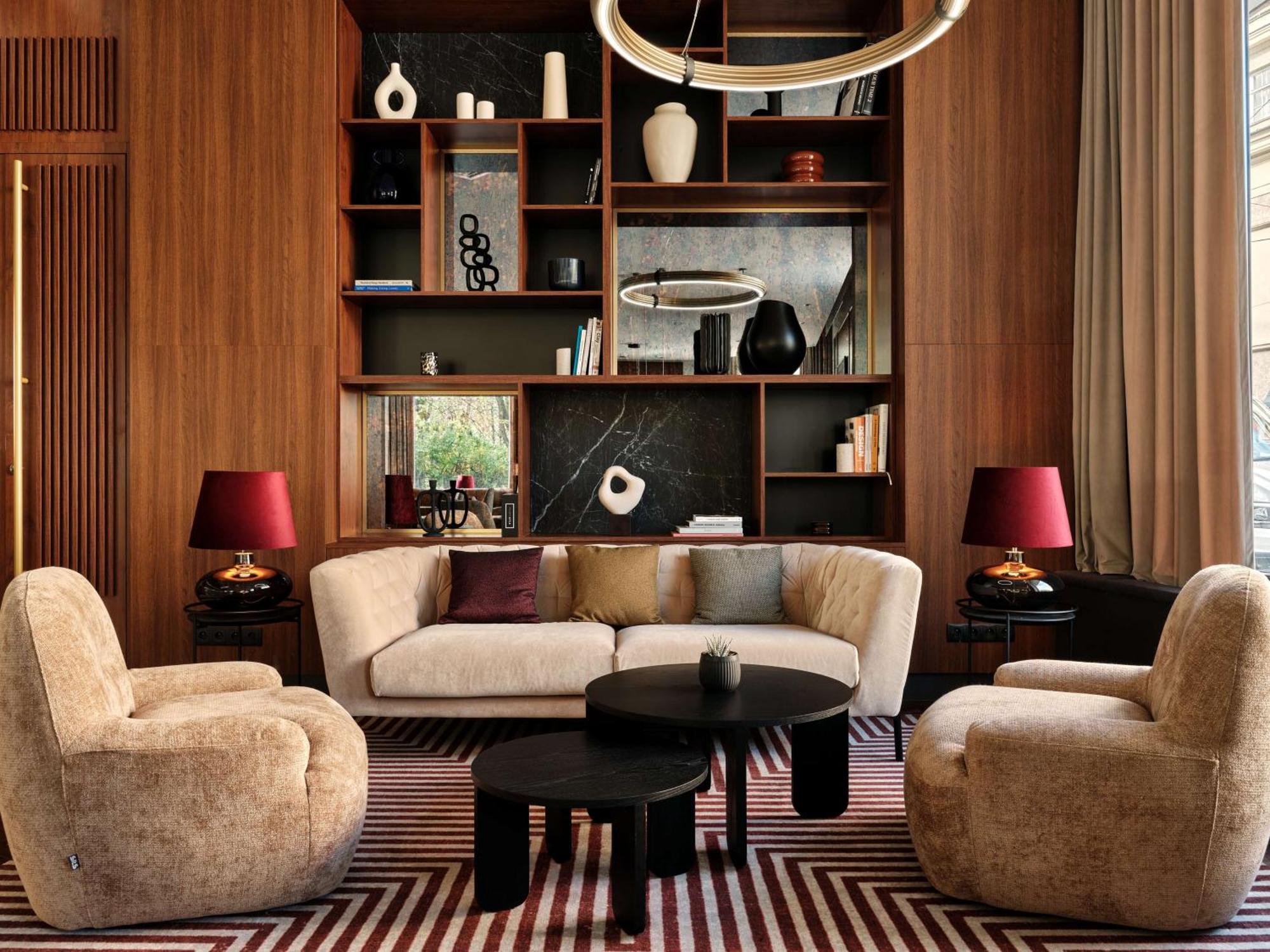 Radisson Blu Hotel Cracovia Esterno foto The image shows a stylish and modern living room space. It features a curved beige sofa centered in the room, accompanied by a round black coffee table. There are two plush armchairs in a similar beige tone positioned across from the sofa. Behind the