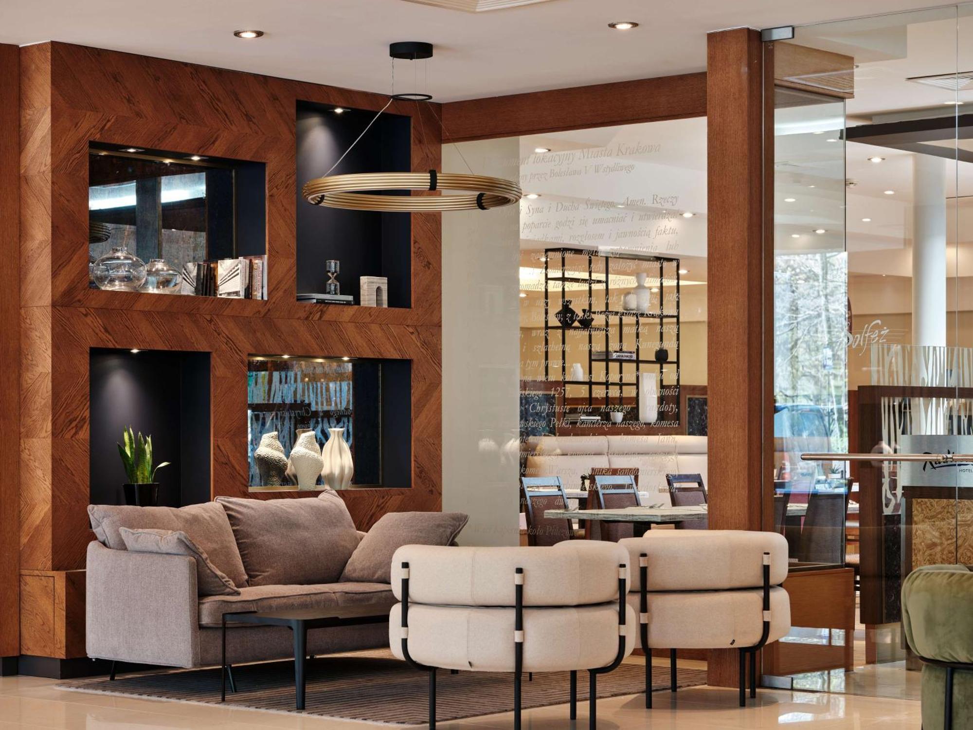 Radisson Blu Hotel Cracovia Esterno foto The photo displays a modern and stylish interior setting, likely from a hotel lobby or a chic lounge area. It features a seating arrangement consisting of a plush gray sofa and two unique chairs that blend comfort and contemporary design. Behind the 