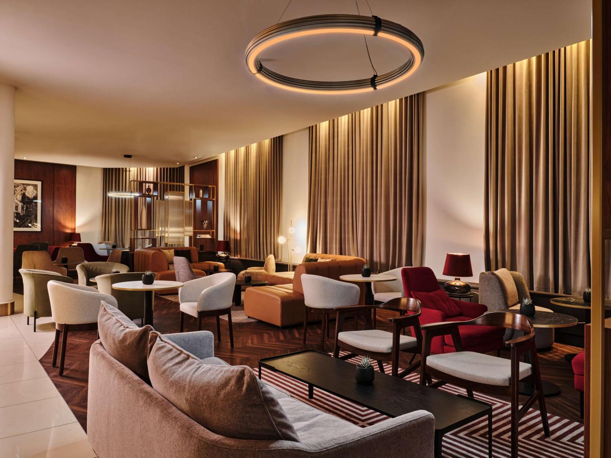 Radisson Blu Hotel Cracovia Esterno foto The photo depicts a modern, stylish lounge area with warm lighting. The space features various seating arrangements, including comfortable sofas and armchairs in different colors and styles. There are elegant tables placed throughout the area, creati