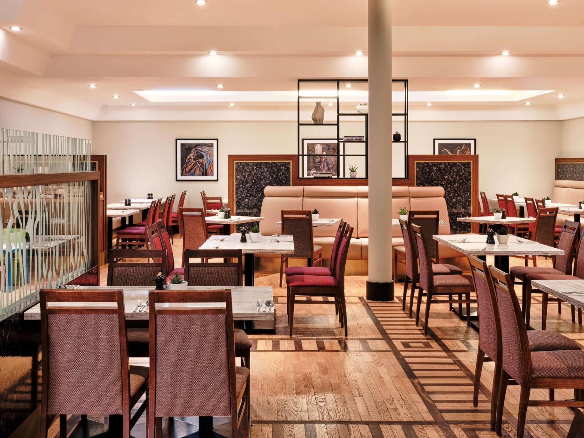 Radisson Blu Hotel Cracovia Esterno foto The photo shows a spacious and modern restaurant interior. There are several tables arranged with chairs, featuring a combination of wooden and fabric elements. The design is elegant, with soft lighting and a neutral color palette. The decor includes
