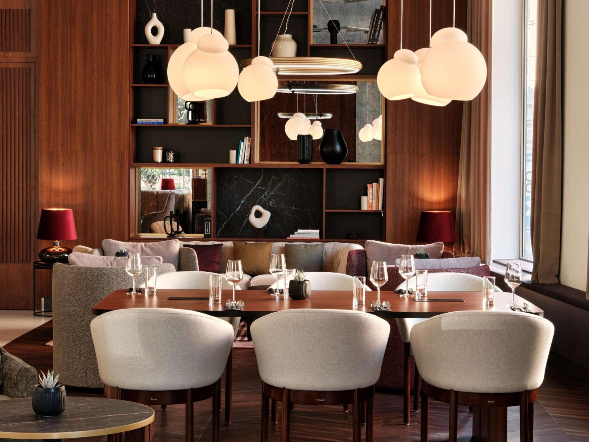 Radisson Blu Hotel Cracovia Esterno foto The photo depicts a stylish and modern dining area. The interior features a sleek wooden wall with built-in shelves displaying decor items and books. The lighting is soft, provided by unique cloud-shaped pendant lights hanging from the ceiling. 

In 