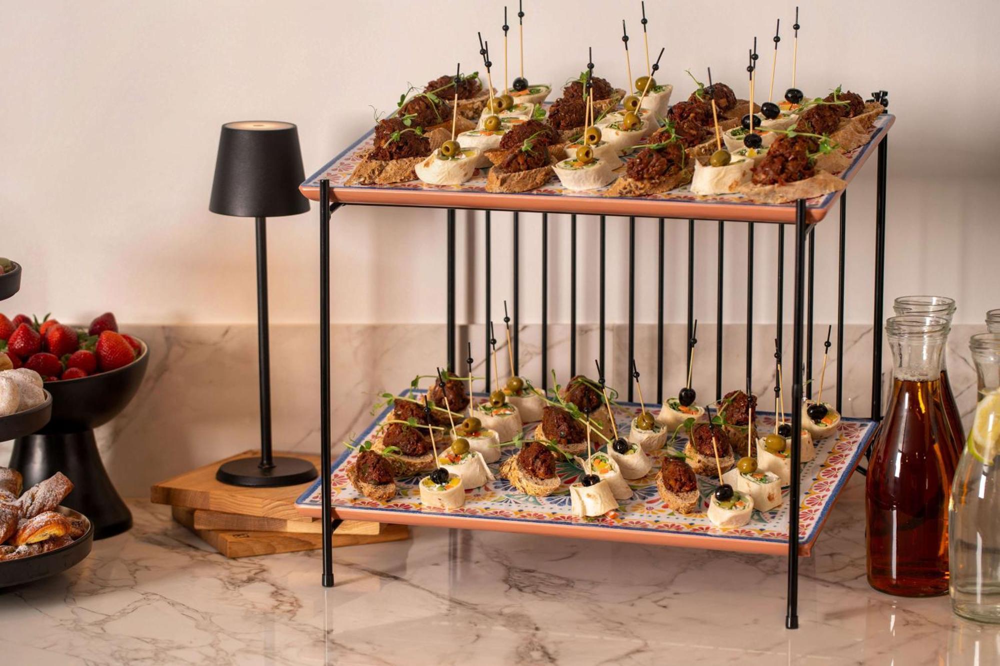 Radisson Blu Hotel Cracovia Esterno foto The image shows a two-tier serving display filled with appetizers. The top and bottom layers feature an assortment of bite-sized food items, likely a mixture of meat and vegetables, artfully presented with decorative toothpicks or skewers. The displa