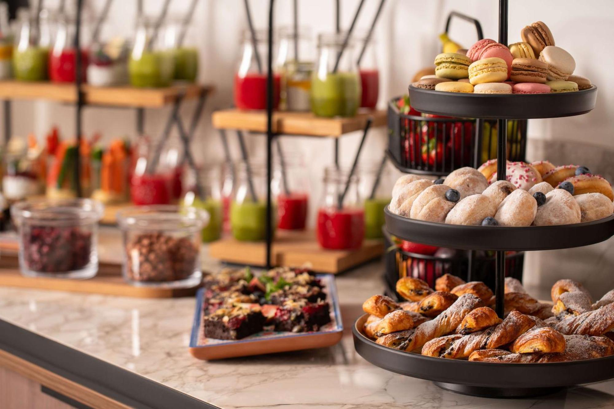Radisson Blu Hotel Cracovia Esterno foto The photo depicts a beautifully arranged buffet spread featuring a variety of food items. In the foreground, there is a tiered stand with an assortment of pastries, including small cakes, cookies, and baked treats. Some of the items appear to be deco
