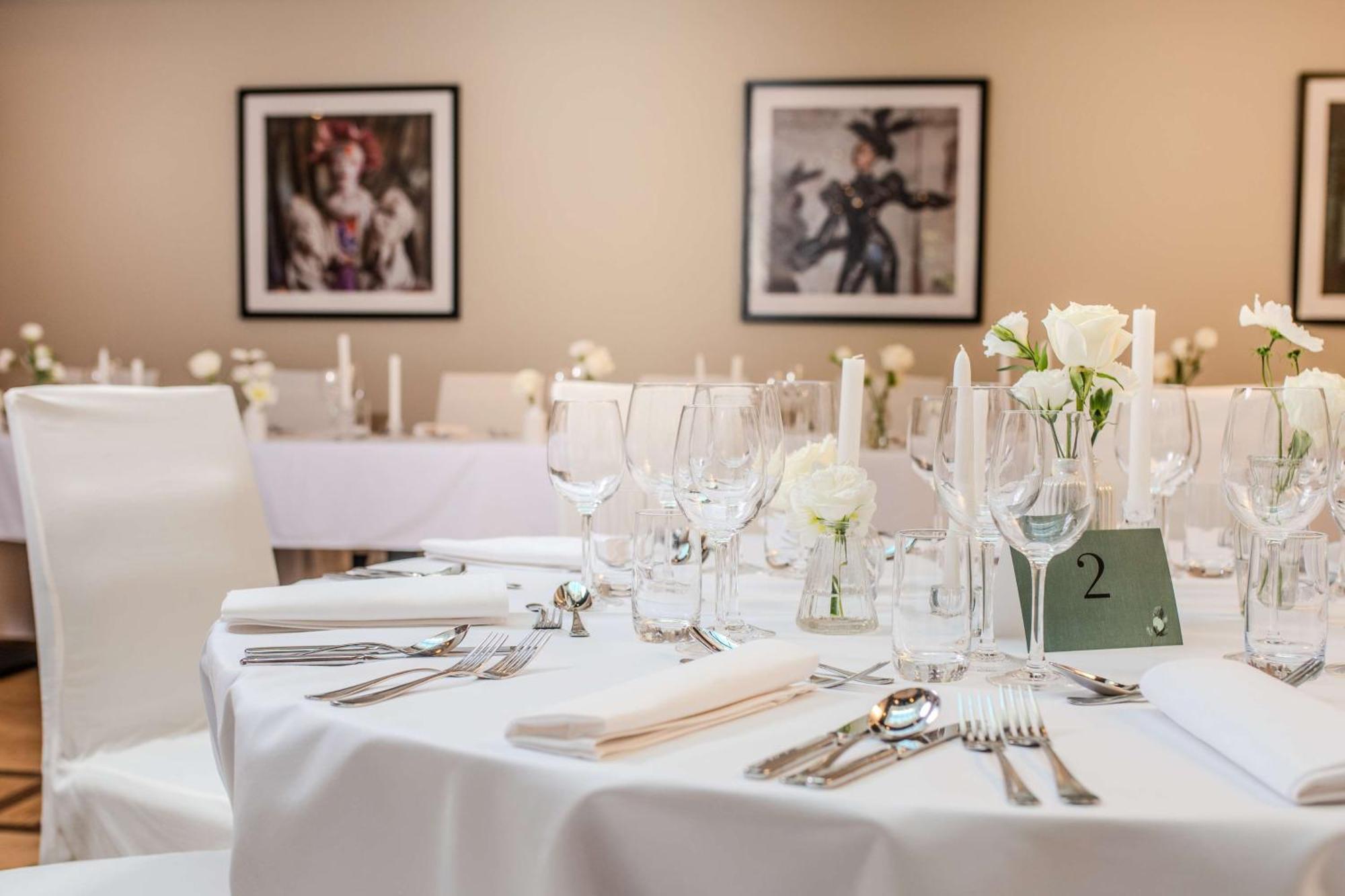 Radisson Blu Hotel Cracovia Esterno foto The photo shows a well-set dining table in a banquet or event space. The table is covered with a white tablecloth and is elegantly arranged with various glassware, including wine glasses and water glasses, alongside neatly placed cutlery. There are s